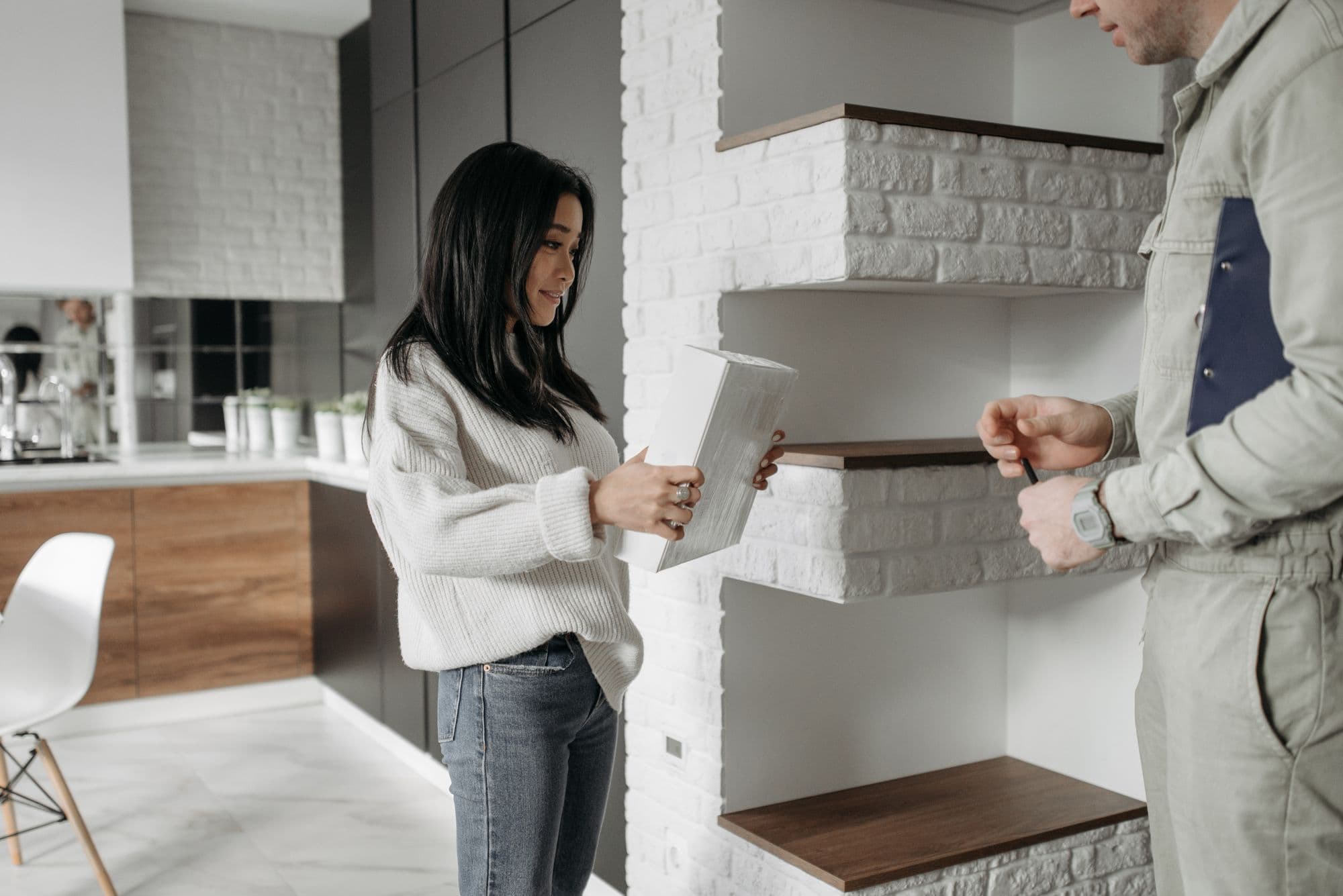Une cliente échange avec un professionnel pendant l'installation d'étagères dans la cuisine.